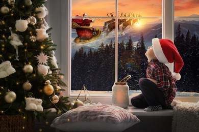 Cute little child on window sill at home waiting for Santa Claus. Christmas celebration
