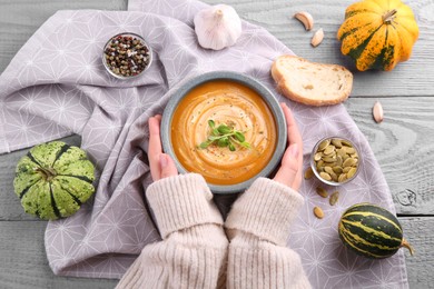 Photo of Woman with bowl of tasty pumpkin soup at grey wooden table, top view