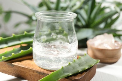 Aloe vera gel in jar and slices of plant on white table, closeup