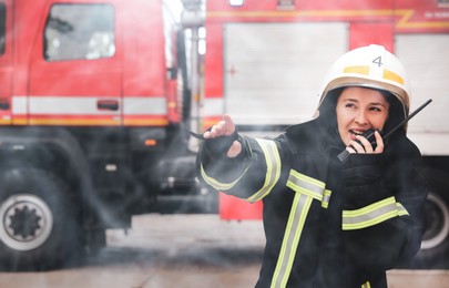 Image of Firefighter in uniform using portable radio set near fire truck outdoors