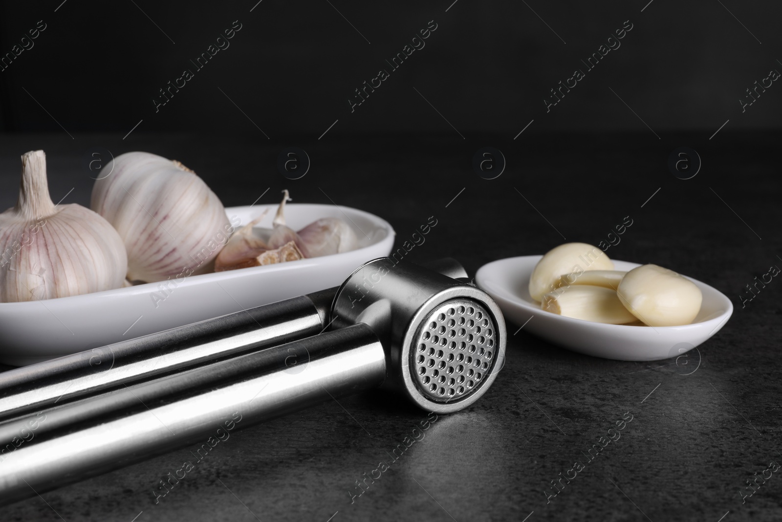 Photo of Garlic press, bulbs and cloves on grey table, closeup