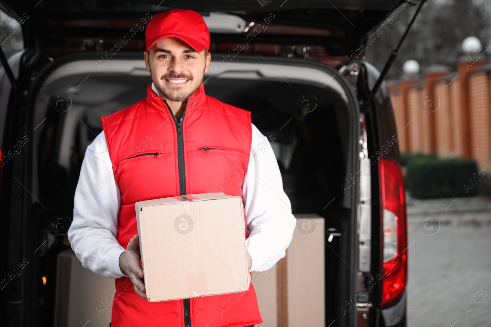 Photo of Deliveryman in uniform with parcel near van outdoors