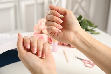 Photo of Woman doing manicure with ultraviolet nail lamp at white table, closeup