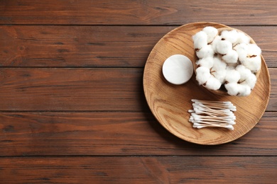 Plate with cotton swabs, pads and flowers on wooden background, top view. Space for text