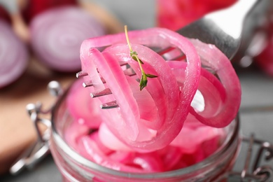 Photo of Fork with tasty pickled onion slices over jar on table, closeup