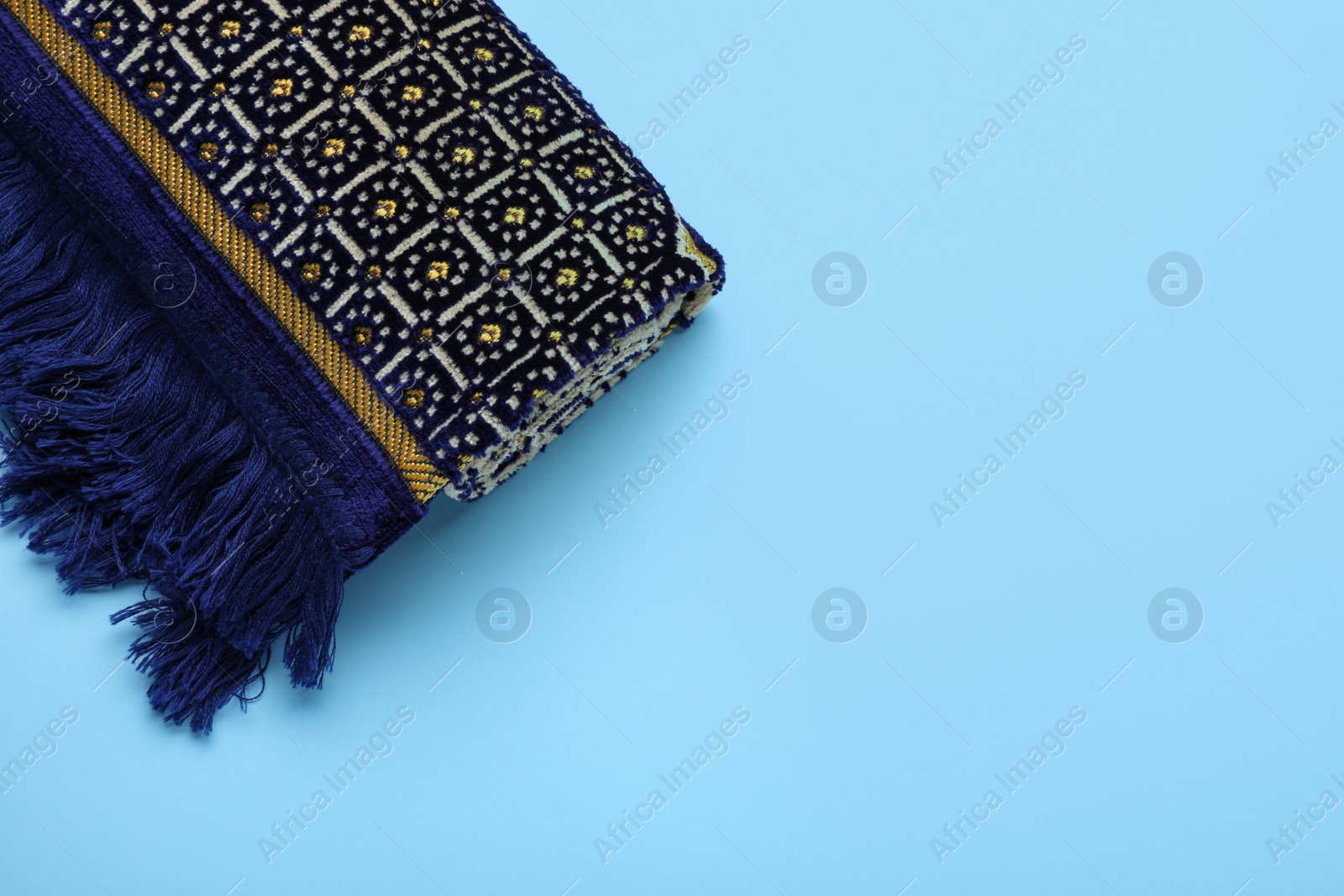 Photo of Muslim prayer rug on light blue background, top view. Space for text