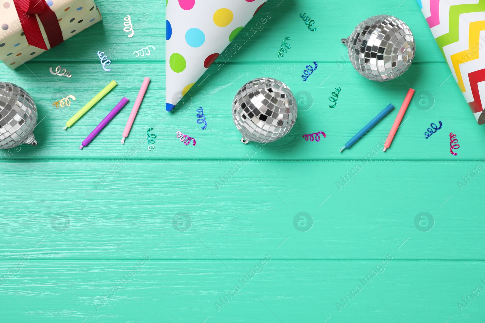 Photo of Shiny disco balls and party decor on turquoise wooden background, flat lay. Space for text