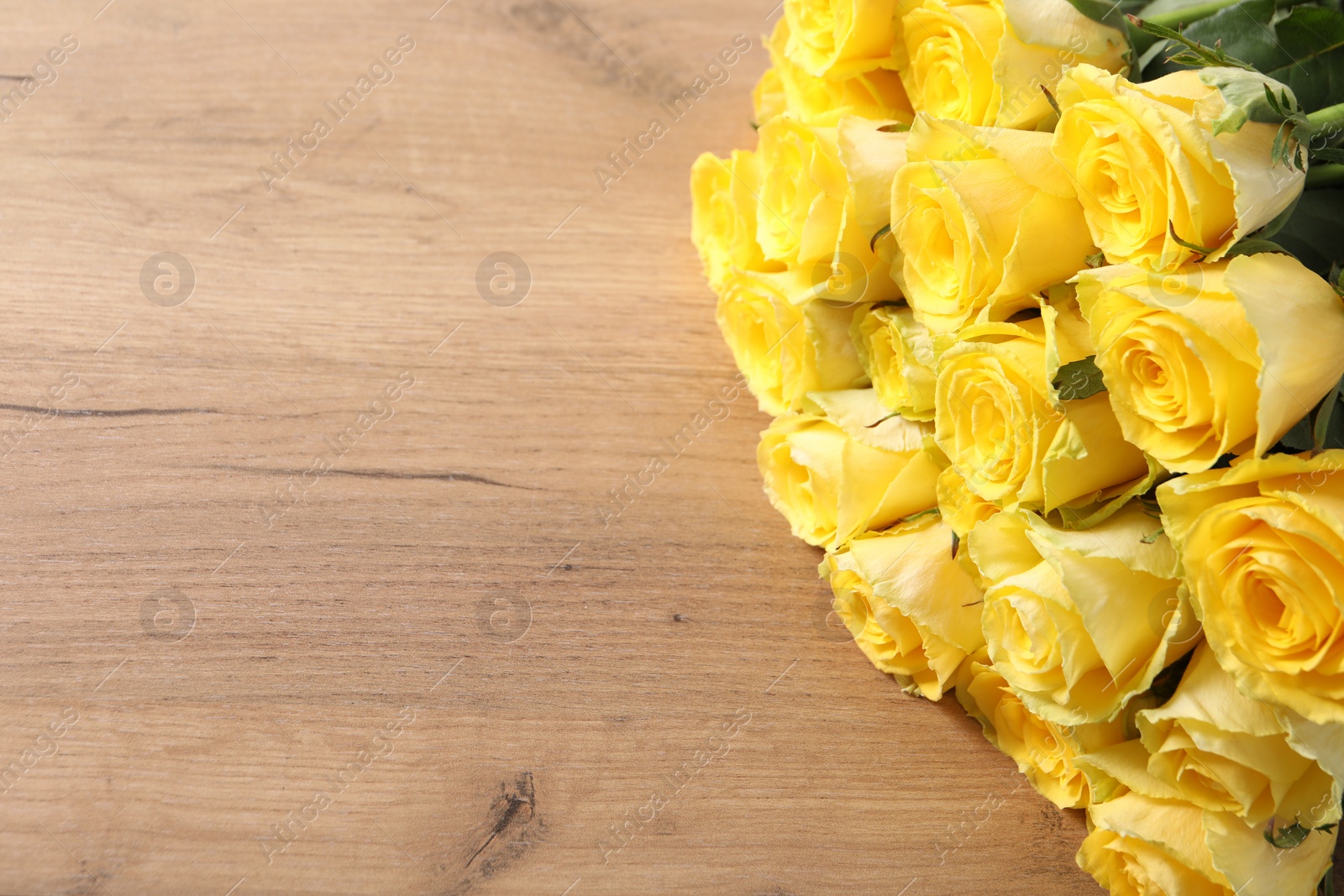 Photo of Beautiful bouquet of yellow roses on wooden table, above view. Space for text