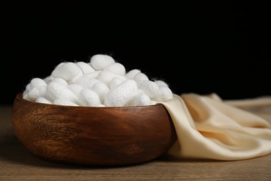 Photo of White cocoons with bowl and silk fabric on wooden table, closeup