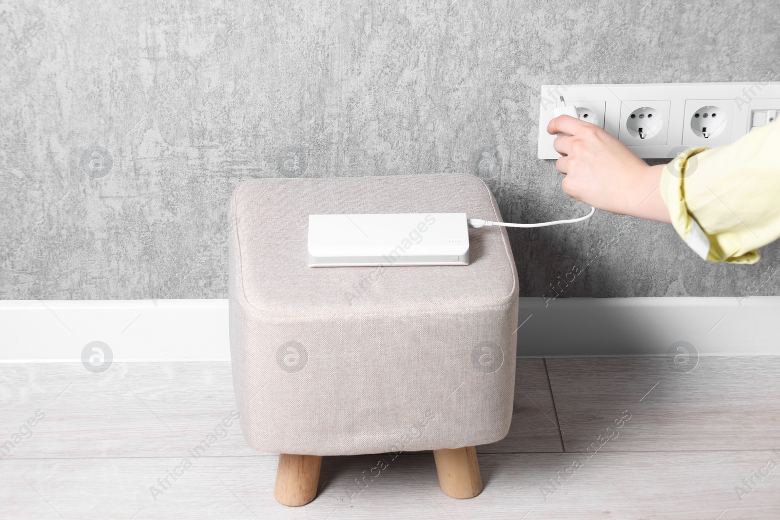 Photo of Woman plugging power bank into socket on grey wall indoors, closeup