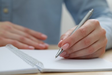 Woman writing with pen in notebook at wooden table, closeup