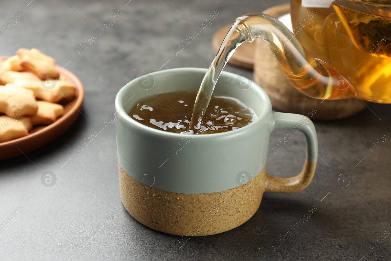 Photo of Pouring tasty tea into cup at grey table indoors, closeup