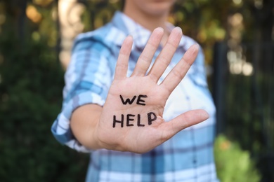 Photo of Woman showing hand with words "WE HELP" outdoors, closeup