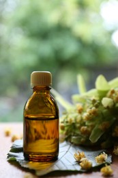 Photo of Bottle of essential oil and linden blossoms on wooden table against blurred background, closeup