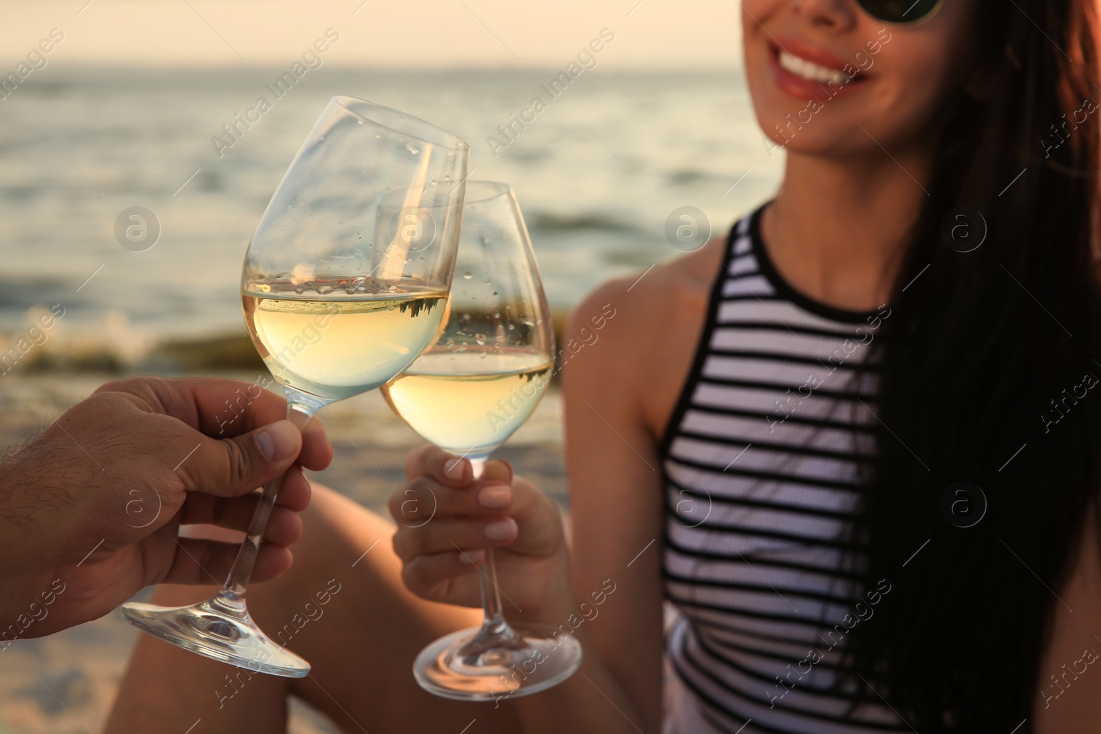 Photo of Lovely couple having picnic near river at sunset, focus on glasses