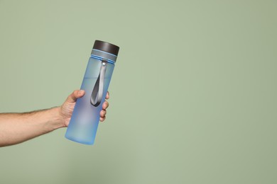 Photo of Man holding transparent plastic bottle of water on light green background, closeup. Space for text