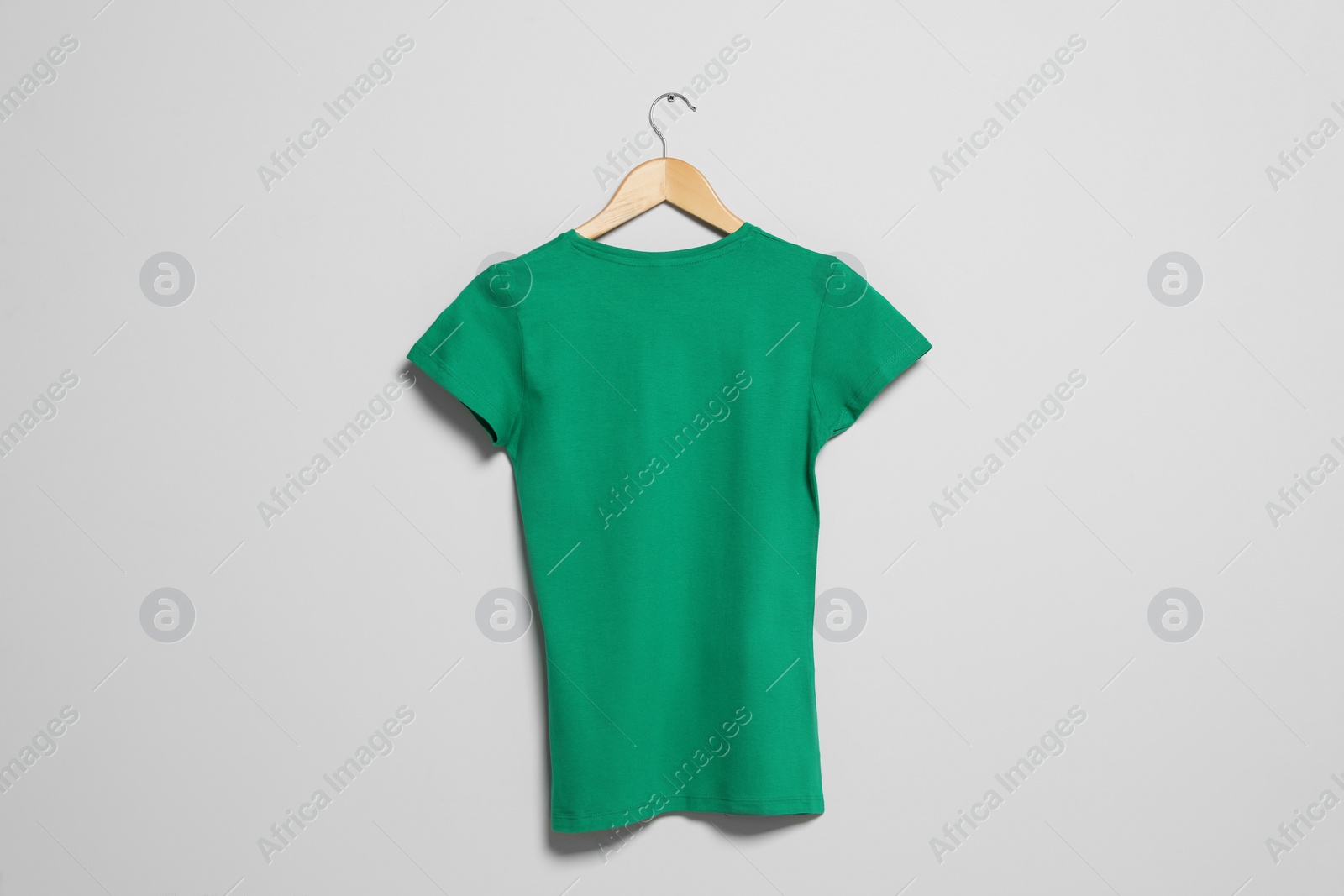 Photo of Hanger with green t-shirt on light wall. Mockup for design