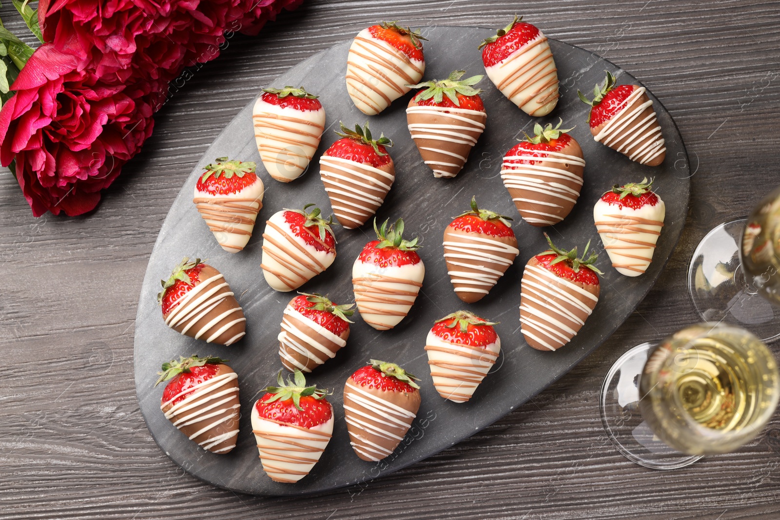 Photo of Delicious chocolate covered strawberries, sparkling wine and flowers on wooden table, flat lay