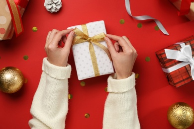 Photo of Woman decorating Christmas gift on red background, top view