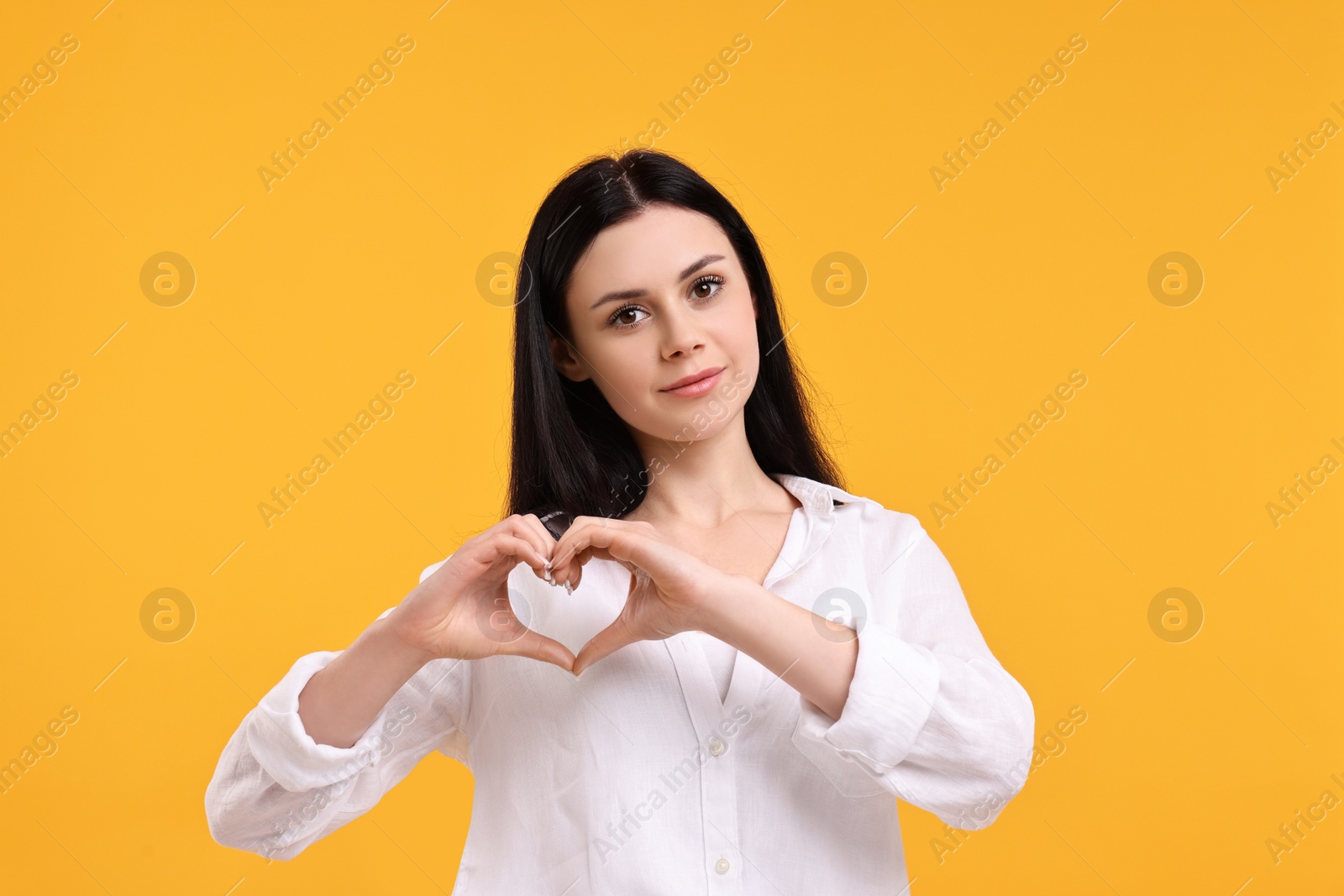 Photo of Beautiful woman showing heart gesture with hands on orange background