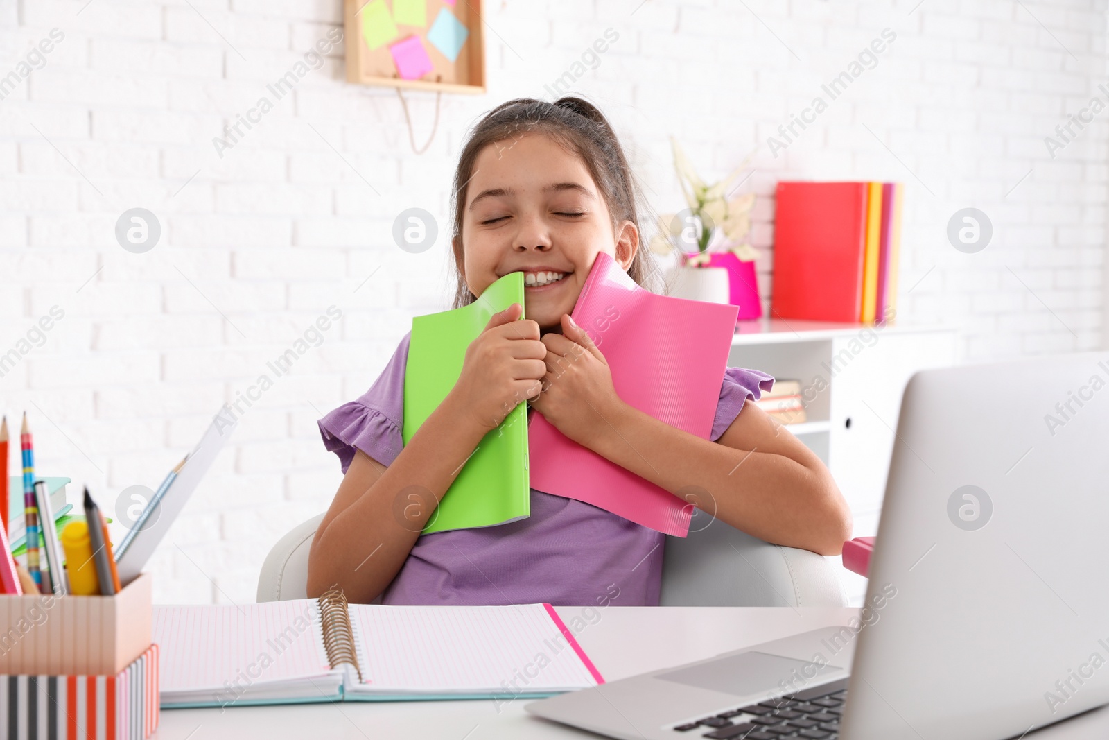 Photo of Happy preteen girl with notebooks at table. Doing homework