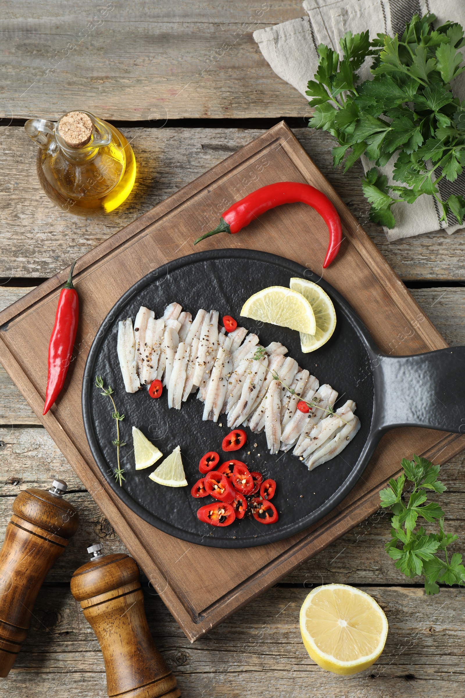 Photo of Tasty anchovies with spices and products on wooden table, flat lay