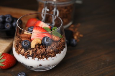 Photo of Tasty granola with berries, nuts and yogurt in glass on wooden table, closeup. Space for text