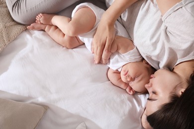 Young mother resting near her sleeping baby on bed, top view. Space for text