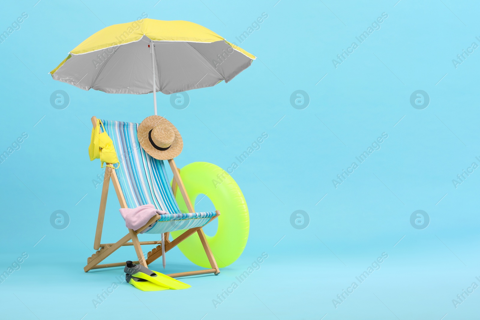 Deck chair, umbrella and beach accessories against light blue background, space for text. Summer vacation Photo of Deck chair, umbrella and beach accessories against light blue background, space for text. Summer vacation