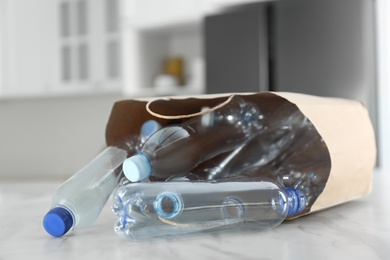 Photo of Paper bag with used plastic bottles on table in kitchen, closeup. Recycling problem