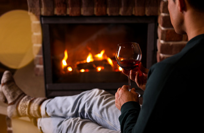 Photo of Man with glass of wine near fireplace at home, closeup