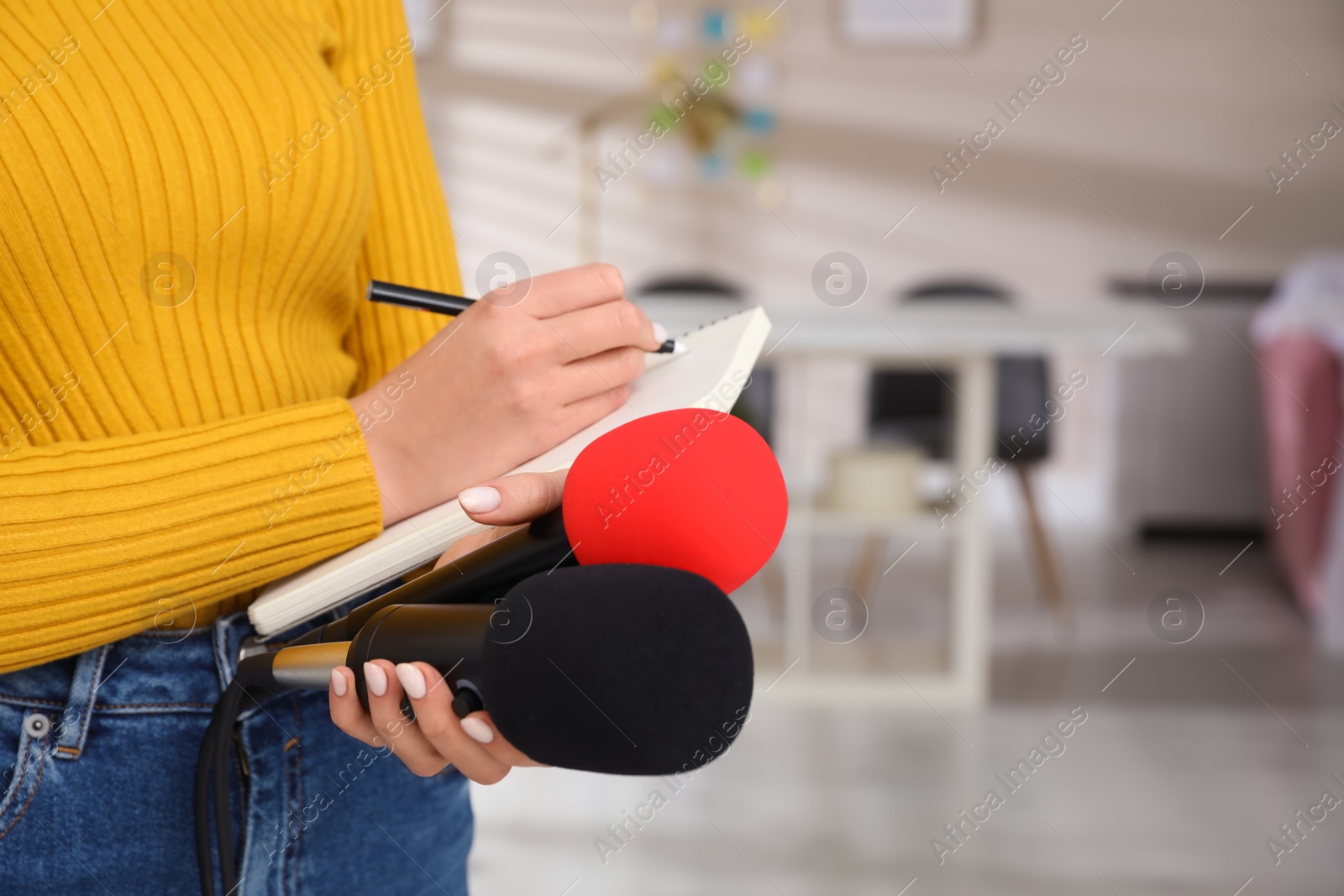 Photo of Professional journalist with microphones taking notes indoors, closeup