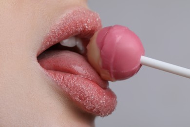Photo of Closeup view of young woman with beautiful lips covered in sugar eating lollipop on light grey background