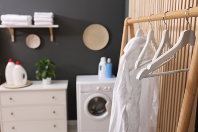 Laundry room interior with washing machine and clothes on rack, selective focus