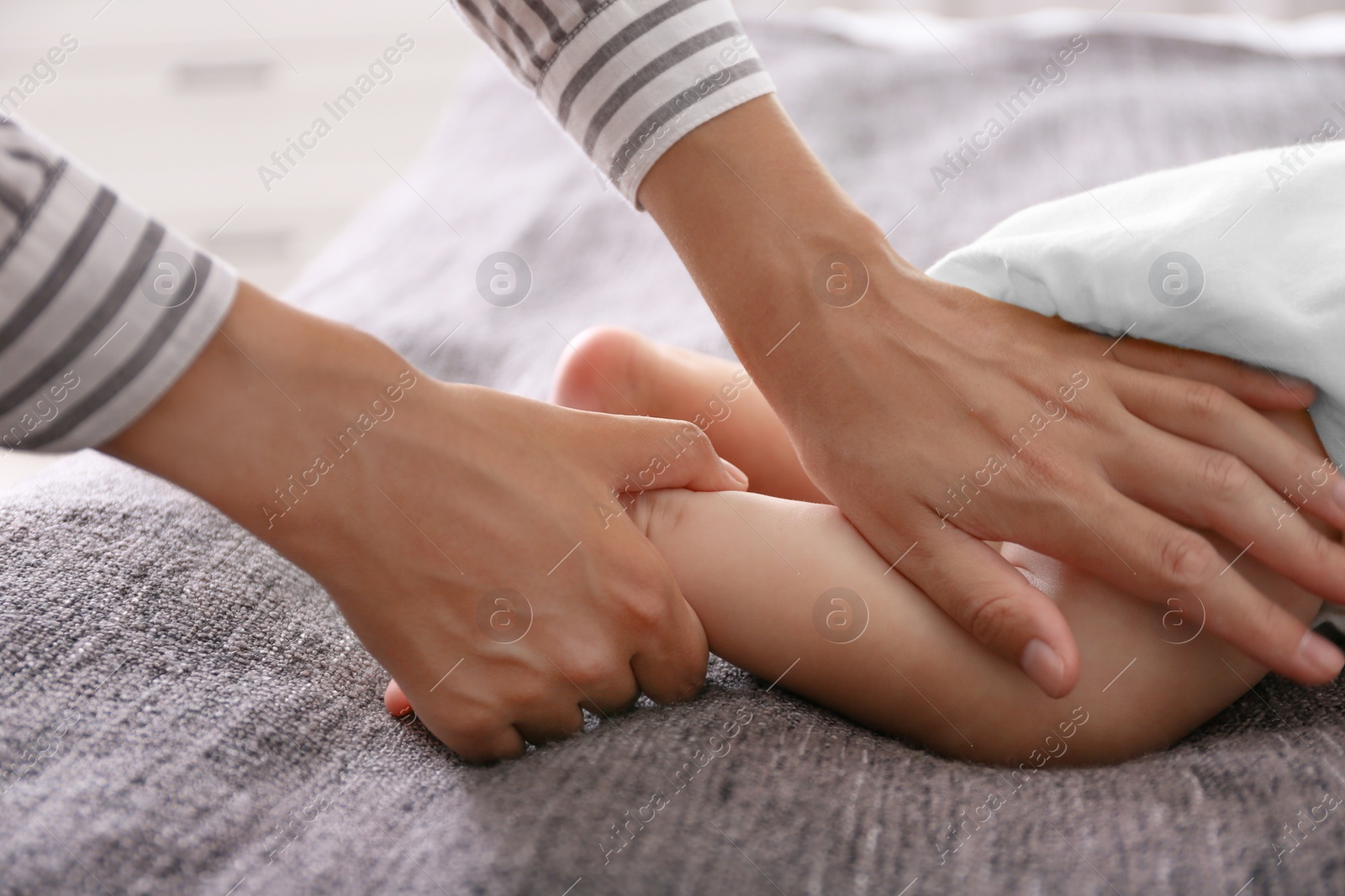 Photo of Woman massaging cute little baby on blanket, closeup