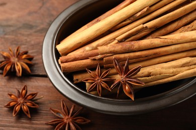 Photo of Bowl with cinnamon sticks and star anise on wooden table, closeup