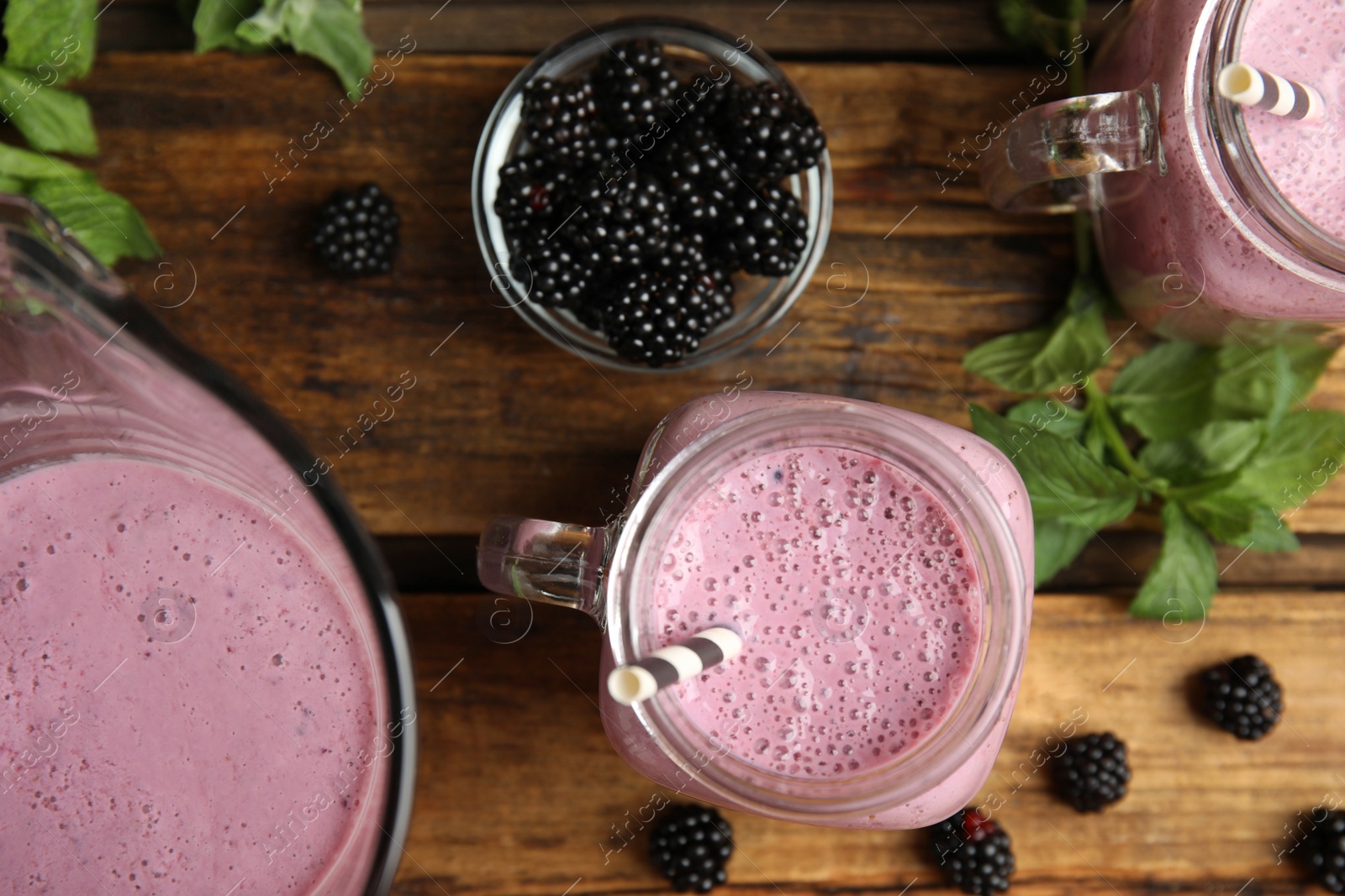 Photo of Tasty fresh milk shakes with blackberries on wooden table, flat lay