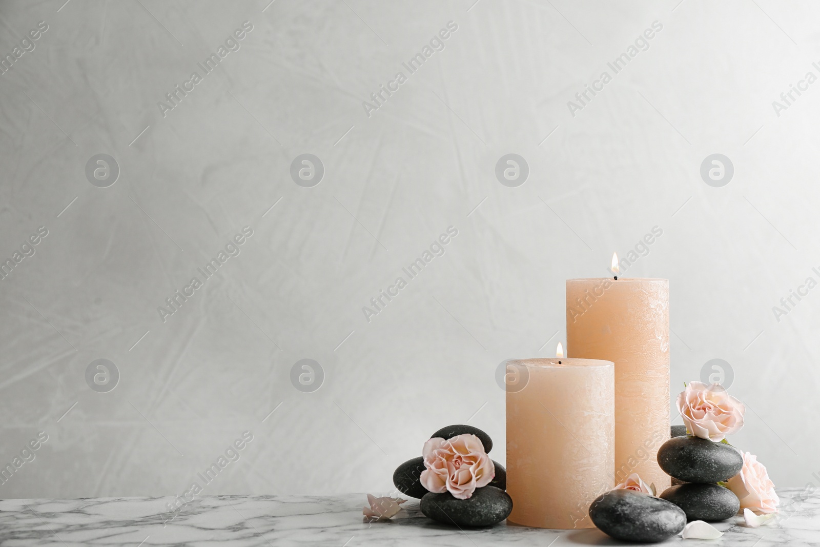 Photo of Composition of burning candles, spa stones and flowers on table. Space for text