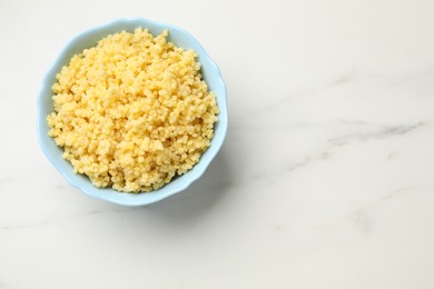 Photo of Tasty millet porridge in bowl on white marble table, top view. Space for text