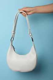 Woman holding stylish white bag on light blue background, closeup