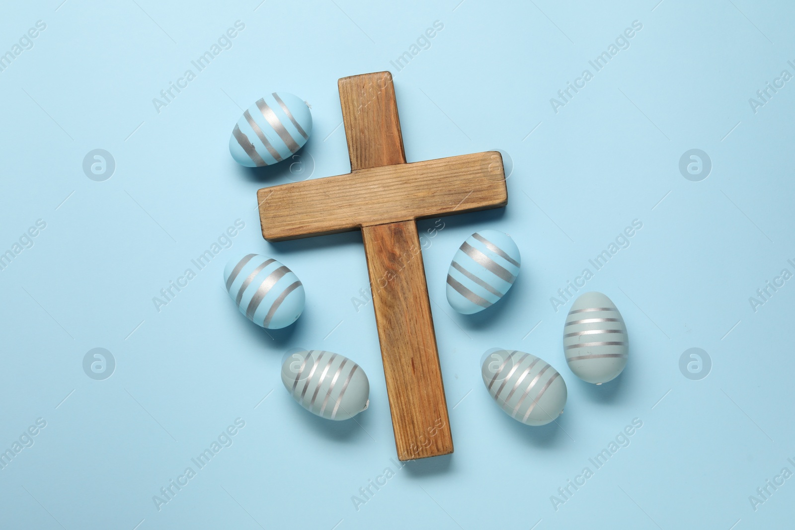 Photo of Wooden cross and painted Easter eggs on light blue background, flat lay