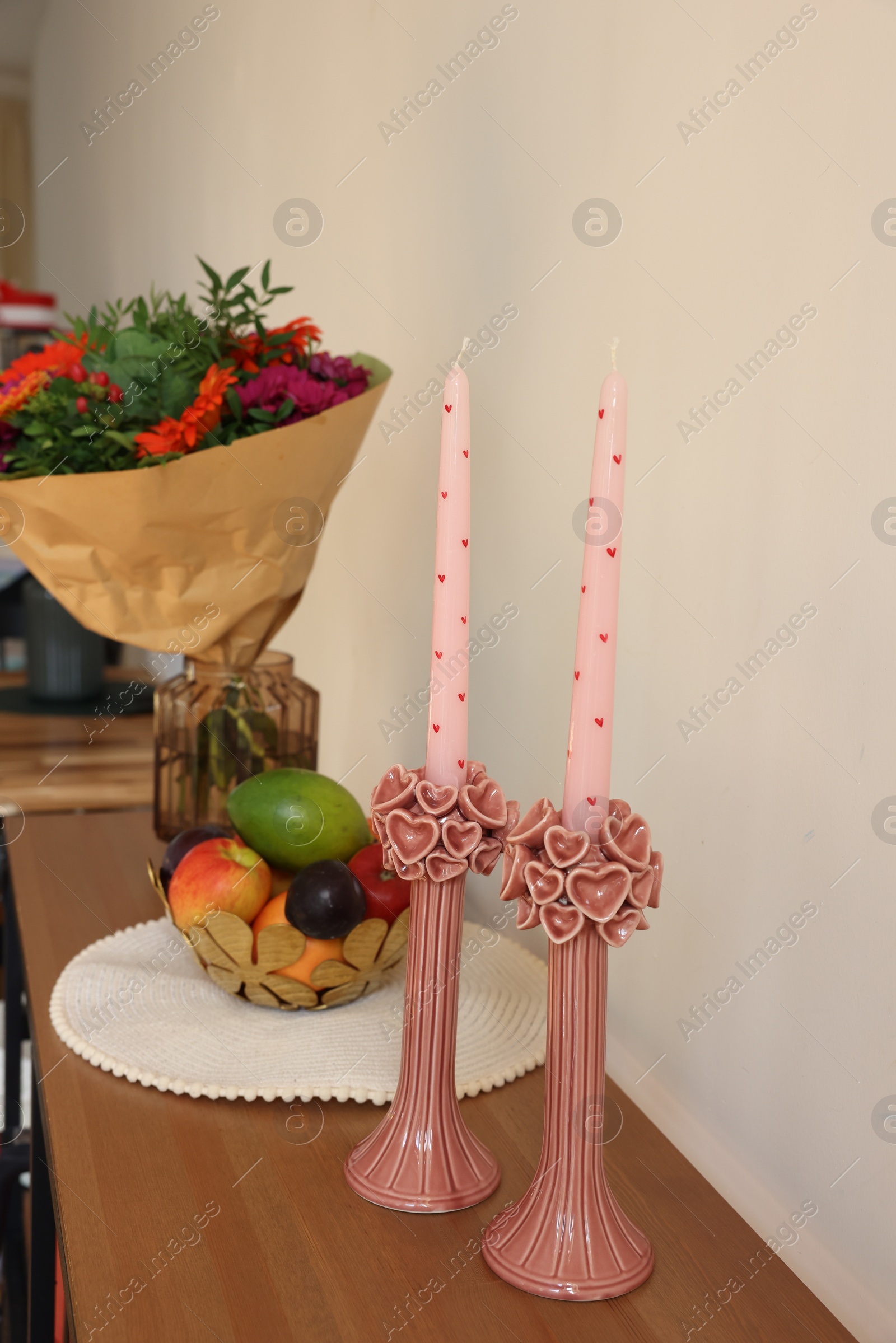 Photo of Bouquet of flowers, bowl with fresh fruits and candles on wooden table near white wall