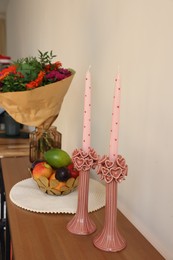 Bouquet of flowers, bowl with fresh fruits and candles on wooden table near white wall