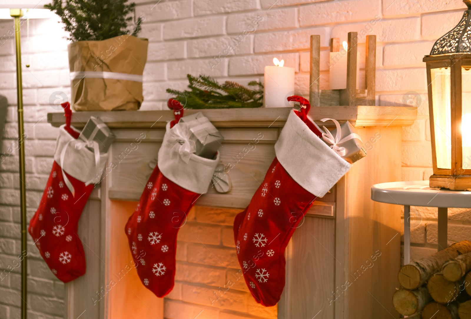 Photo of Red Christmas stockings with gifts on decorative fireplace indoors. Festive interior