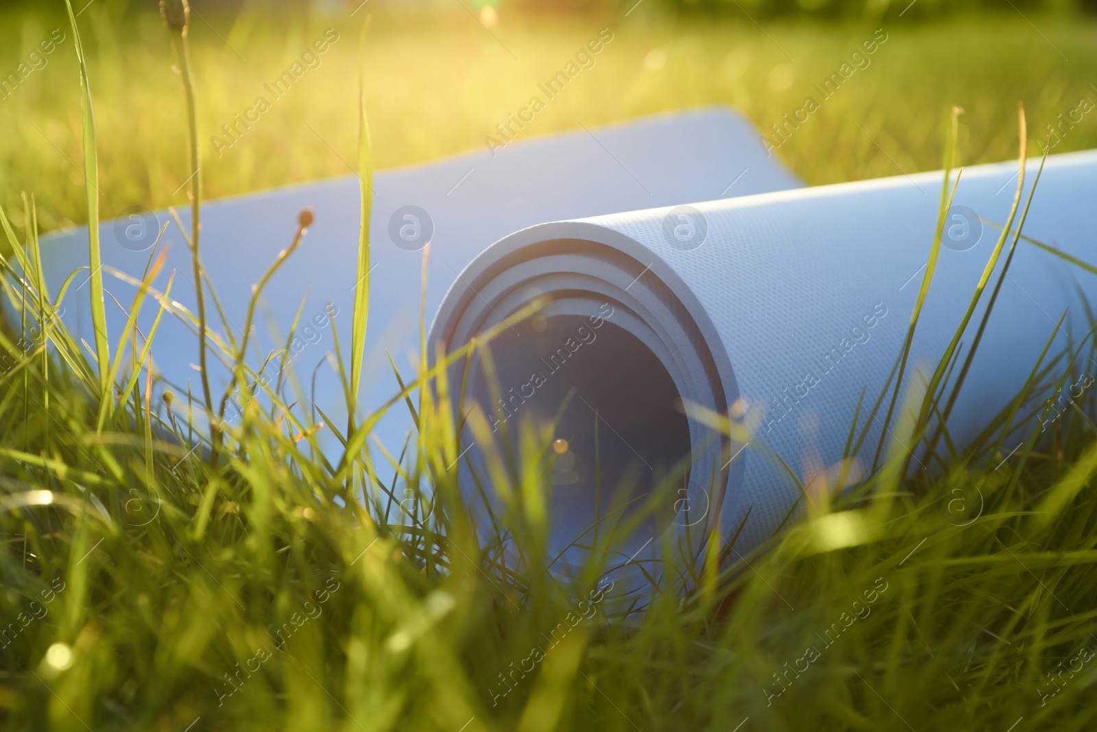 Photo of Blue karemat or fitness mat in fresh green grass outdoors, closeup