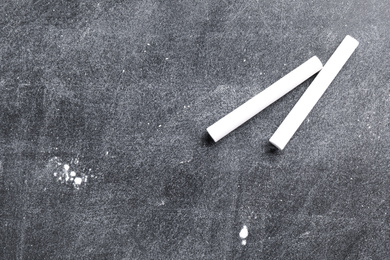 Photo of Pieces of white chalk on blackboard, flat lay. Space for text