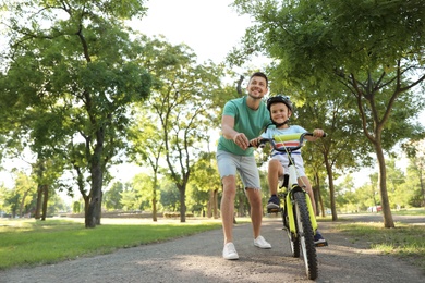 Photo of Happy father teaching his son to ride bicycle in park