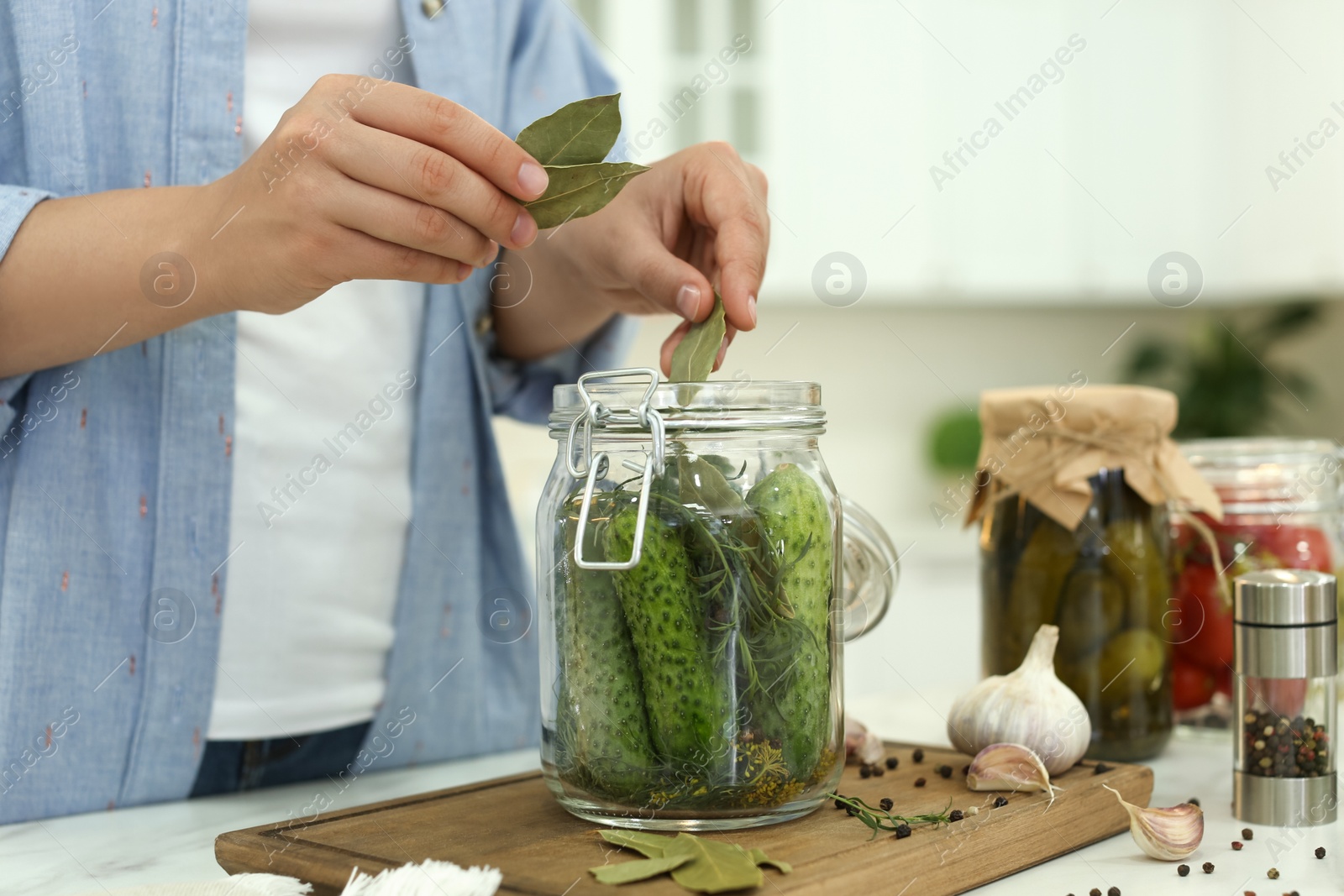 Photo of Woman putting bay leaves into pickling jar at table in kitchen, closeup