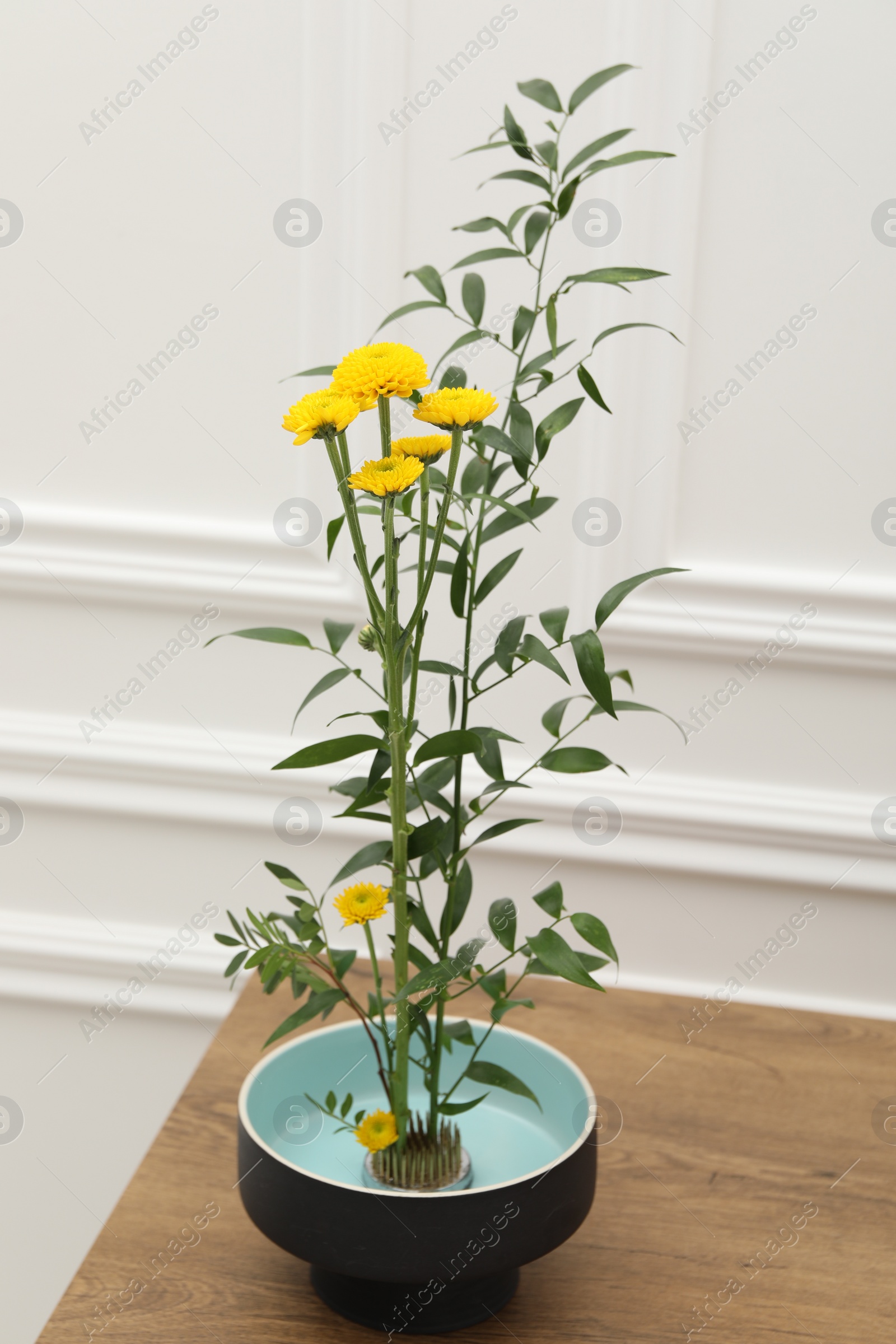 Photo of Ikebana art. Beautiful yellow flowers and green branch carrying cozy atmosphere at home