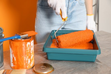 Woman taking orange paint with roller from tray at table, closeup